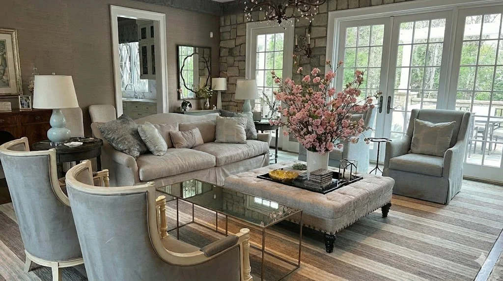 A bright living room with a beige sofa, light armchair and glass doors opening to a patio.