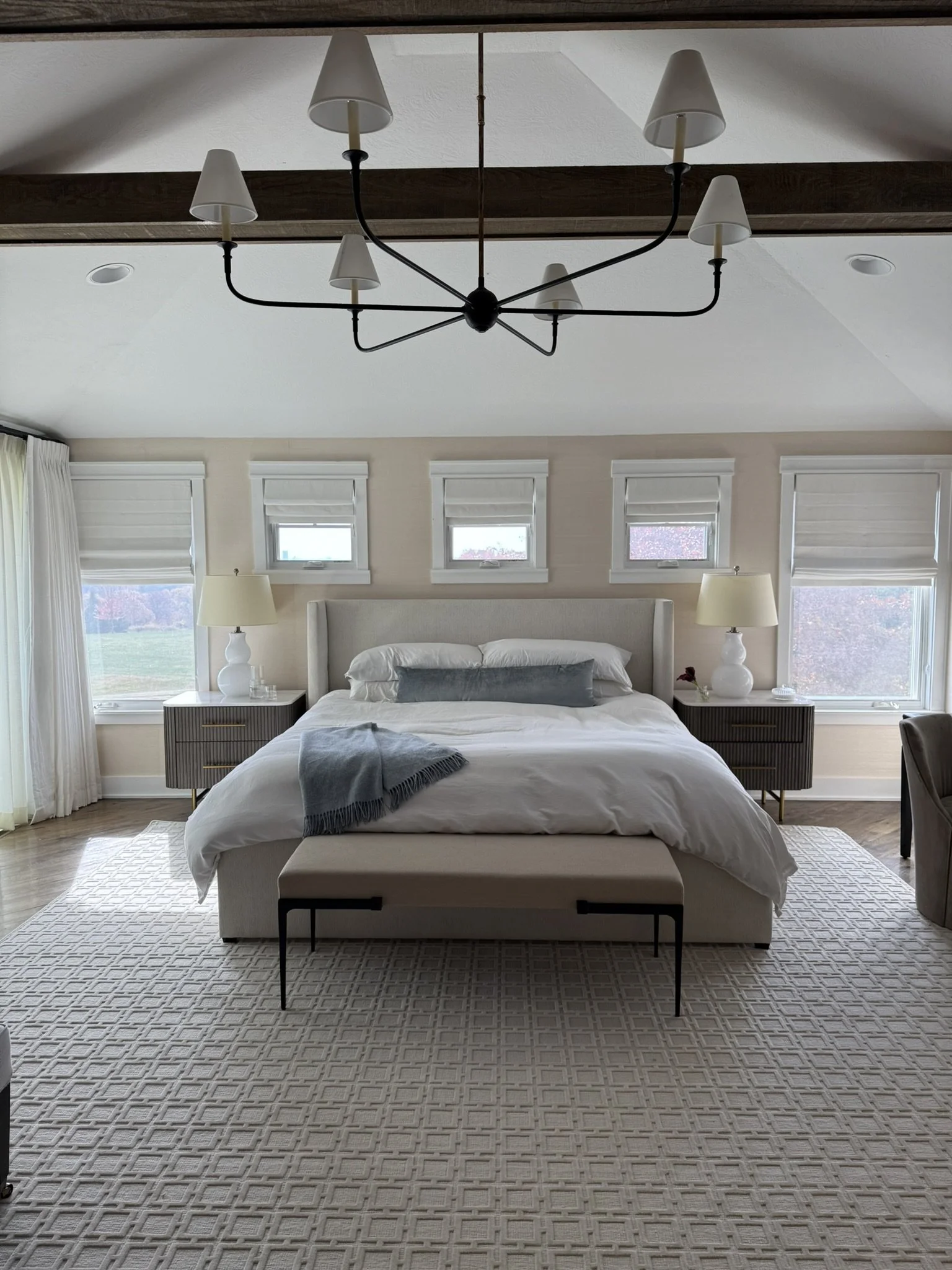 A bedroom with white bedding, matching nightstands and small windows above the headboard.