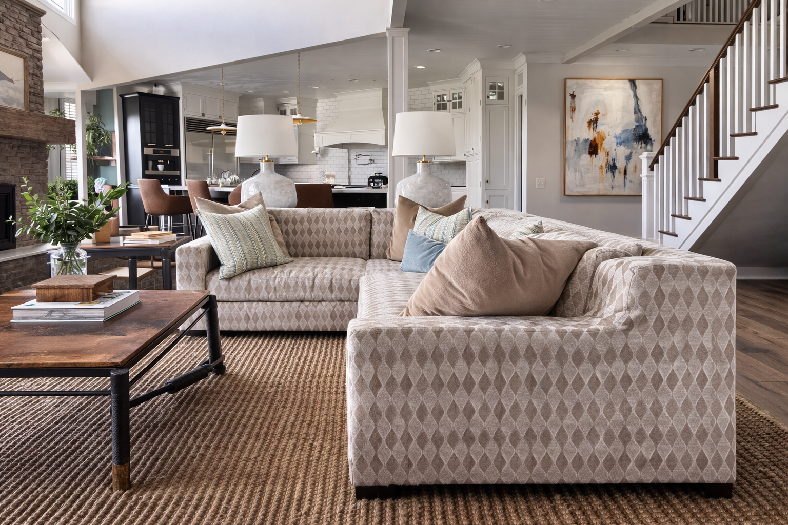 A living room with a beige sectional, decorative pillows and an open kitchen beyond.
