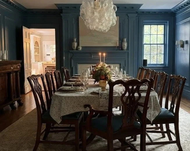 Formal dining room with deep blue walls, a long table set with fine china, a chandelier and a fireplace.