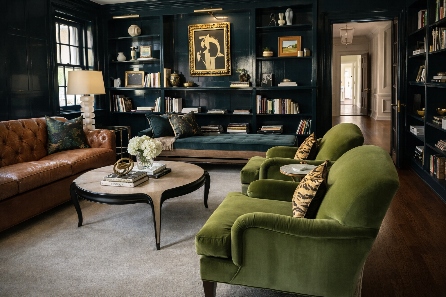 A library with lacquered blue walls, built-in bookshelves, green velvet armchairs and a camel leather sofa.