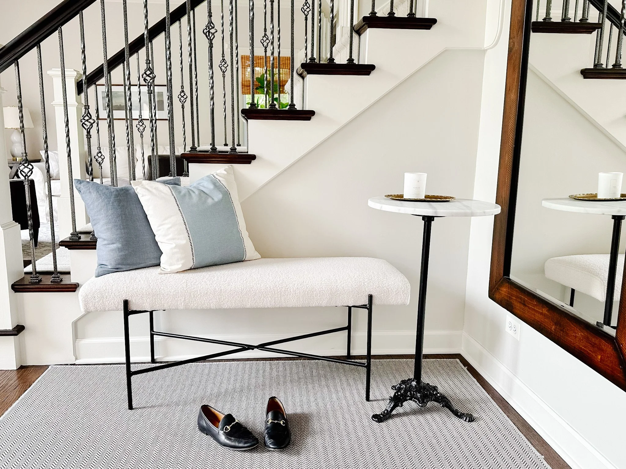 An entryway with a cushioned bench, a marble-topped table and a large wooden-framed mirror.