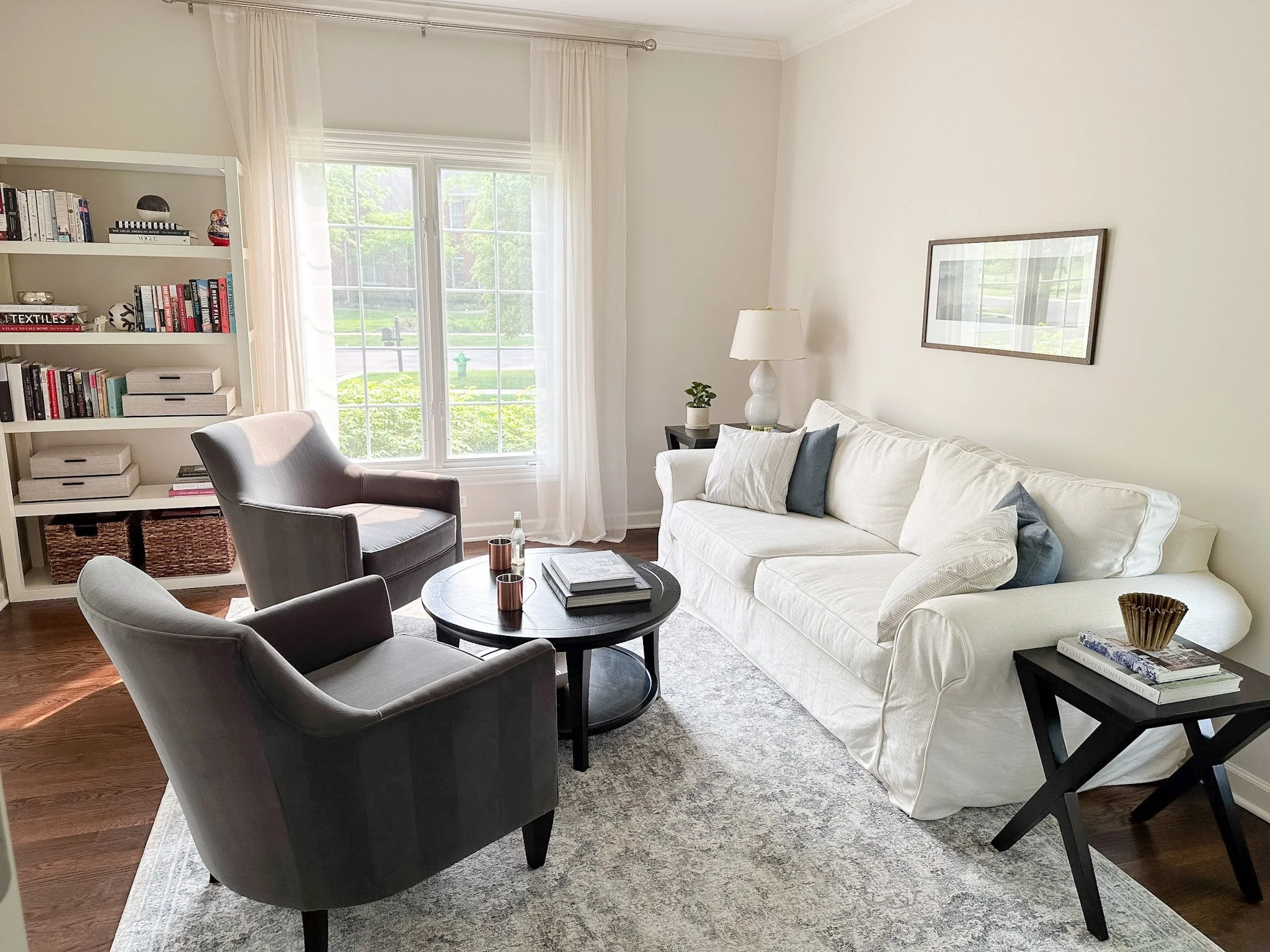 A finished living room with a slipcovered white sofa, two velvet armchairs, a round coffee table and styled bookshelves.