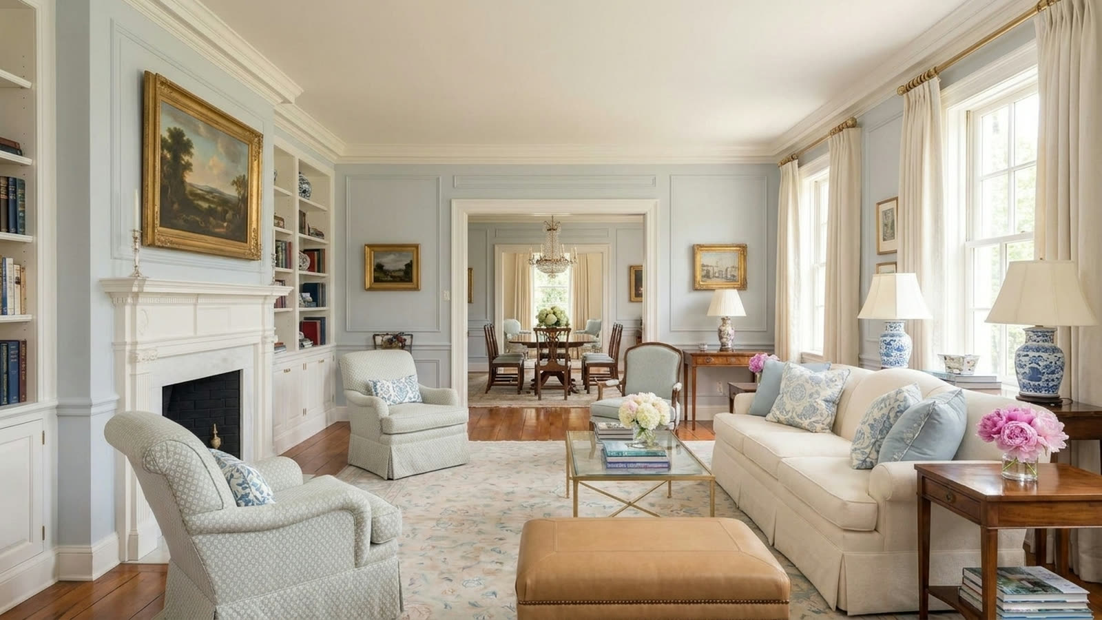 A living room with pale blue-grey walls, a cream sofa, pale patterned armchairs, a brass and glass coffee table and an antique floral rug.